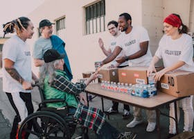 Volunteers distribute bottled water and supplies to diverse individuals in an outdoor setting, showcasing community support.